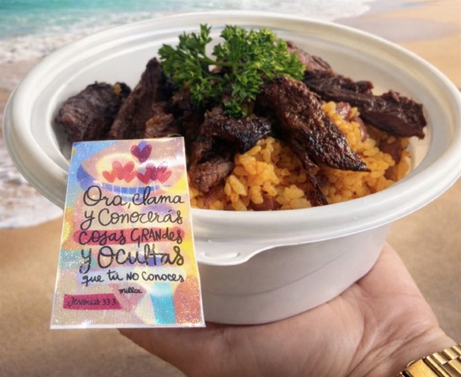 Bowl con arroz y trozos de churrasco, sostenido en la playa junto a una tarjeta de versículo.